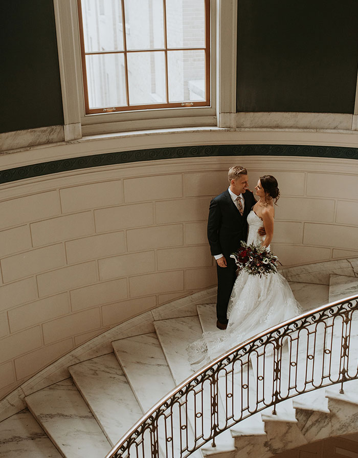 Bride and groom stand on spiral staircase while embracing